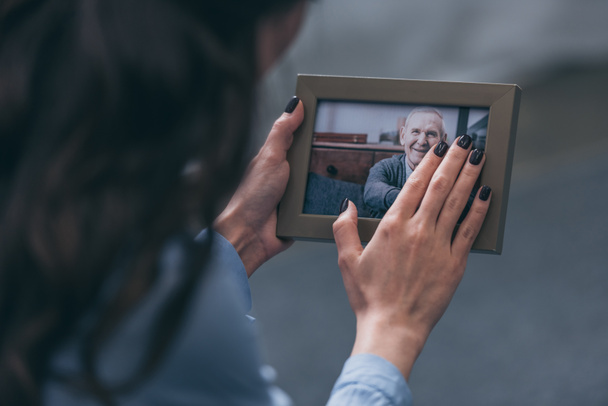 Ausgeschnittene Ansicht einer Frau, die einen Fotorahmen mit einem reifen Mann zu Hause hält, Konzept der Trauerstörung - Foto, Bild