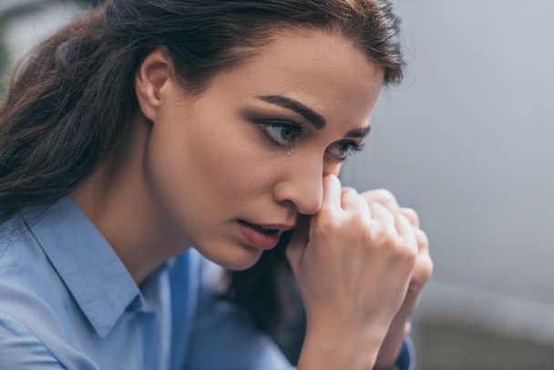 Portret van triest huilende vrouw in blauwe blouse in kamer, rouwende stoornis concept - Foto, afbeelding