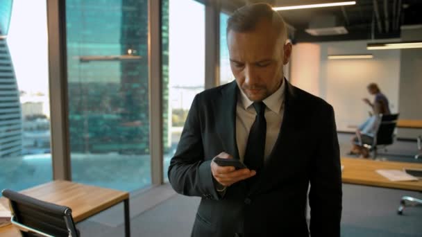 Handsome man standing near window writing sms. He looking very confident and smart, controlling his employees at office. 4k glidetrack slider middle shot. - Metraje, vídeo