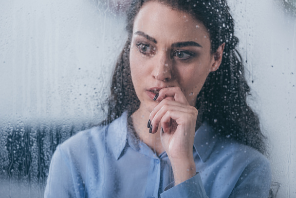 beautiful upset woman touching face and looking through window with raindrops - Фото, изображение