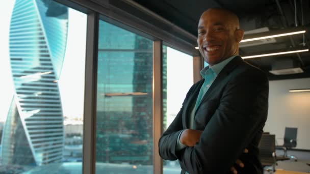 Africano chefe americano de pé perto de enorme janela de escritório moderno e sorrisos
. - Filmagem, Vídeo