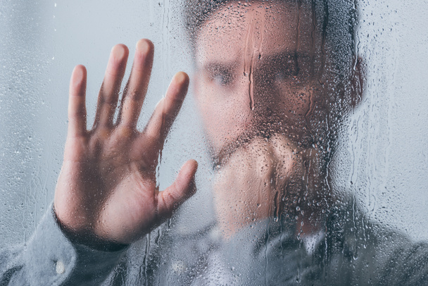 boos man die betrekking hebben op mond met de hand en raken venster met regendruppels - Foto, afbeelding