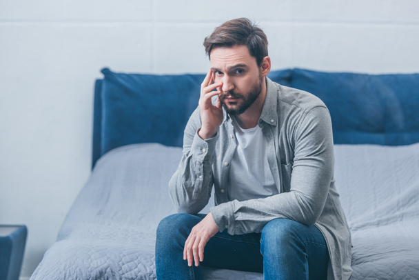 depressed man sitting on bed, looking at camera and grieving at home - Foto, Bild