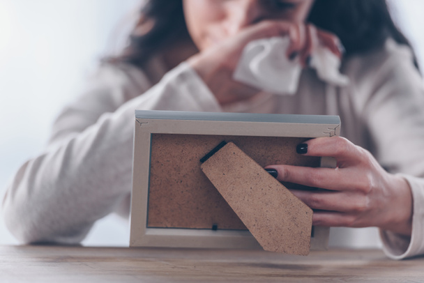 обрезанный вид расстроенной женщины, держащей рамку и плачущей дома
 - Фото, изображение