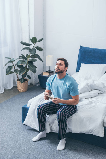 grieving man sitting on bed, looking up and holding photo frame at home - Photo, Image