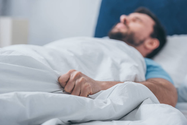 man in bed liggen en houden van de deken - Foto, afbeelding