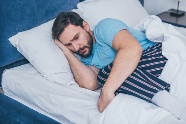 sad man in pajamas grieving while lying in bed alone - Photo, Image