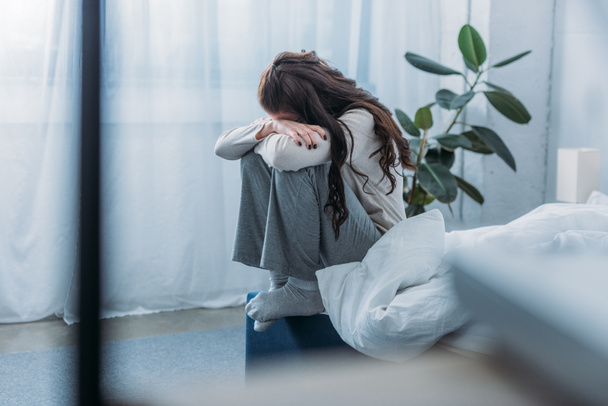 mujer afligida sentada, cubriendo la cara con las manos y llorando en el dormitorio
 - Foto, imagen