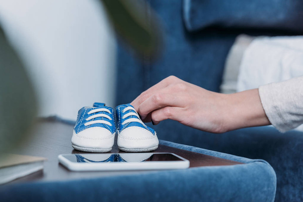 cropped view of woman holding baby shoes at home - Фото, изображение