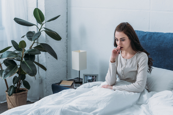 красивая депрессивная женщина лежит в постели и кусает палец
 - Фото, изображение