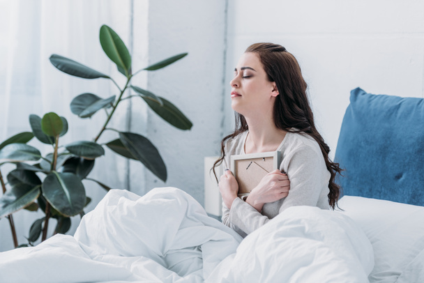 mujer afligida con los ojos cerrados en la cama sosteniendo el marco de la imagen en casa
 - Foto, Imagen