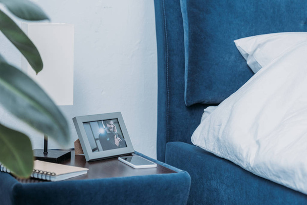 selective focus of photo frame with picture of man, notebook and smartphone on bedside table - Foto, Imagem