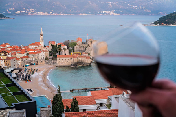 Donna che tiene il bicchiere con il vino rosso sul balcone del suo appartamento nella città di Budva, Montenegro
 - Foto, immagini