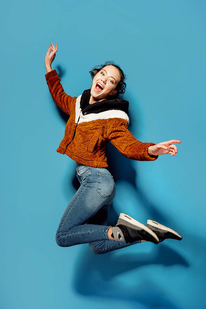 Young woman in casual jumping in air over blue background - Zdjęcie, obraz