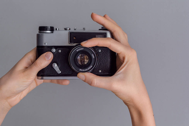Γυναικεία χέρια που κρατούν κάμερας ρετρό φωτογραφία στο φόντο γκρίζο τοίχο - Φωτογραφία, εικόνα