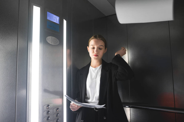 Memnun işkadını kağıtları asansörde atıyor. Şikayetçi ofis çalışanı okuma ve belgeleri asansörde atma. - Fotoğraf, Görsel