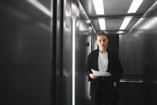 Una mujer de negocios ambiciosa y pensativa está en el ascensor y tratando de recordar algo. Empleada desconcertada está pensando en los documentos de retención del ascensor
. - Foto, Imagen