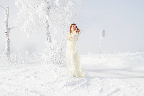 Red-haired young girl on the background of snow-covered trees. Winter portrait - Foto, Bild