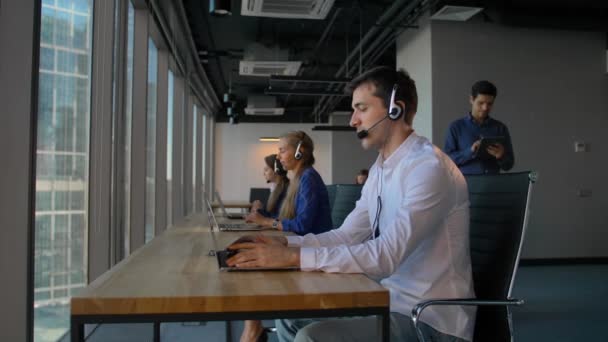 Homme en chemise utilisant un casque avec ordinateur portable tout en travaillant dans le bureau du centre d'appels
 - Séquence, vidéo