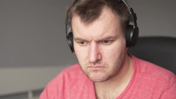 Een ernstige man hoofdtelefoon zit op een stoel achter de computer - Video