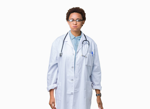 Mladý americký lékař žena nosí lékařský plášť přes izolované pozadí nafoukla tváře s legrační obličej. Ústa naplněny vzduchem, šílený výraz. - Fotografie, Obrázek