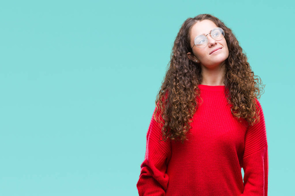 Beautiful brunette curly hair young girl wearing glasses and winter sweater over isolated background smiling looking side and staring away thinking. - Foto, immagini