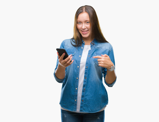 Jeune belle femme caucasienne textos envoi message en utilisant smartphone sur fond isolé avec visage surprise pointant vers lui-même
 - Photo, image