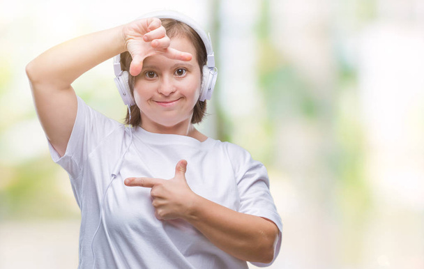 Mladé dospělé ženy s Downovým syndromem nošení sluchátek izolované pozadí provedení rámu s rukama a prsty s šťastné tváře. Koncept kreativity a Fotografie. - Fotografie, Obrázek