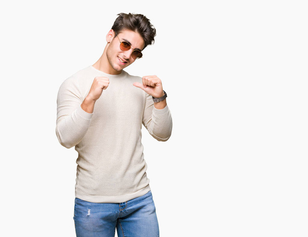 Jonge knappe man dragen van een zonnebril op geïsoleerde achtergrond op zoek vertrouwen met glimlach op het gezicht, wijzen zichzelf met de vingers trots en blij. - Foto, afbeelding