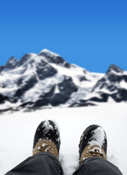 El excursionista en un paisaje de montaña de invierno. Zapatilla de senderismo en las piernas.Turista descansando en la nieve en los Alpes suizos
. - Foto, Imagen