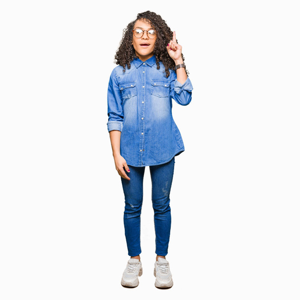 Young beautiful woman with curly hair wearing glasses pointing finger up with successful idea. Exited and happy. Number one. - Foto, imagen