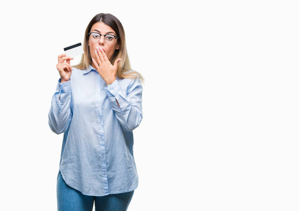 Young beautiful business woman holding credit card over isolated background cover mouth with hand shocked with shame for mistake, expression of fear, scared in silence, secret concept - Fotografie, Obrázek