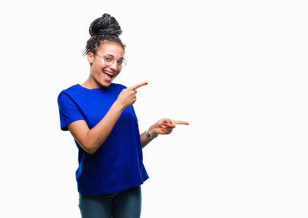 junge geflochtene Haare afrikanisches amerikanisches Mädchen mit Brille über isoliertem Hintergrund lächelnd und mit zwei Händen und Fingern zur Seite in die Kamera blickend. - Foto, Bild