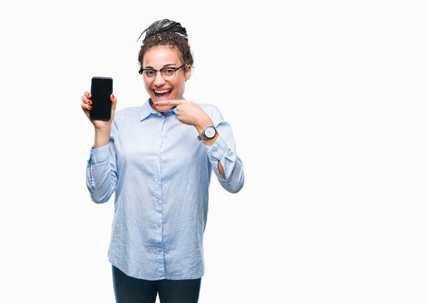 Young gevlochten haar Afrikaanse Amerikaanse bedrijfsleven meisje weergegeven: scherm van de smartphone over geïsoleerde achtergrond erg blij met de hand en de vinger te wijzen - Foto, afbeelding