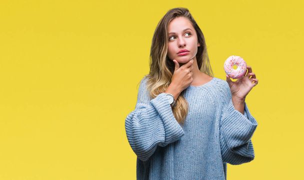 Young beautiful blonde woman eating sweet donut over isolated background serious face thinking about question, very confused idea - Foto, immagini