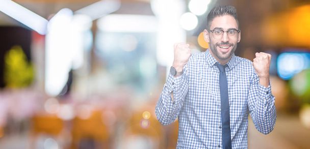 Young business man wearing glasses over isolated background celebrating surprised and amazed for success with arms raised and open eyes. Winner concept. - Photo, Image