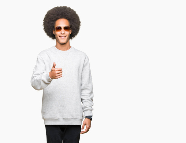 Giovane uomo afro-americano con i capelli afro indossare occhiali da sole facendo pollici felici in alto gesto con la mano. Approvazione espressione guardando la fotocamera con successo mostrando
. - Foto, immagini