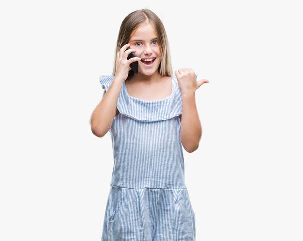 Young beautiful girl talking on the phone over isolated background pointing and showing with thumb up to the side with happy face smiling - Φωτογραφία, εικόνα