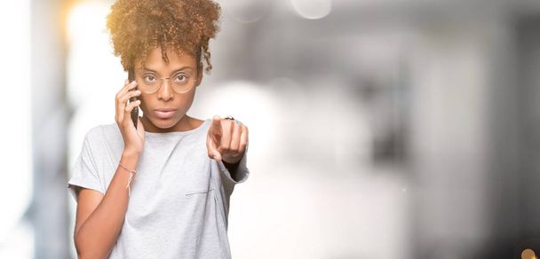 Jeune femme afro-américaine parlant sur smartphone sur fond isolé pointant du doigt la caméra et vers vous, signe de la main, geste positif et confiant de l'avant
 - Photo, image