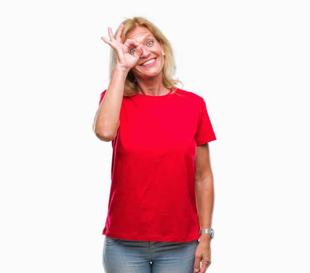 Μέσης ηλικίας ξανθιά γυναίκα απομονωμένη φόντο κάνει εντάξει χειρονομία με το χέρι, χαμογελώντας, το μάτι ψάχνει μέσα από τα δάχτυλα με χαρούμενο πρόσωπο. - Φωτογραφία, εικόνα