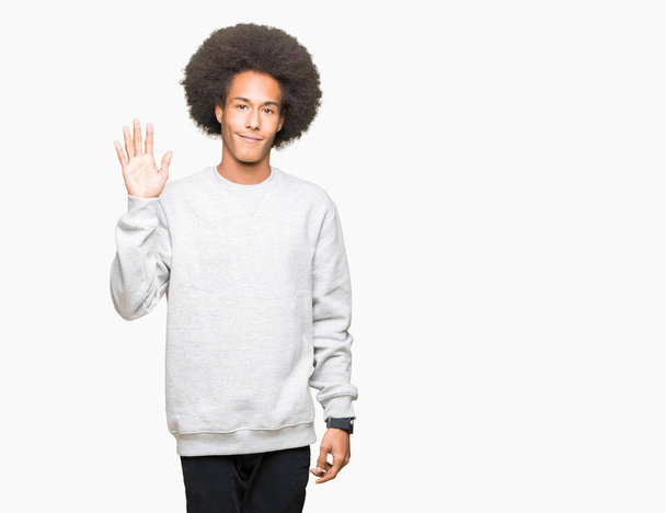 Jonge Afro-Amerikaanse man met afro haar dragen sportieve sweater afzien zeggen Hallo gelukkig en lachende, vriendelijke Welkom gebaar - Foto, afbeelding