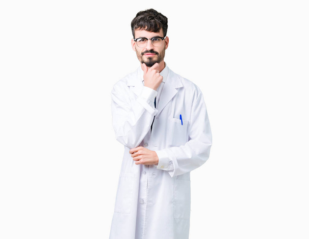 Young professional scientist man wearing white coat over isolated background looking confident at the camera with smile with crossed arms and hand raised on chin. Thinking positive. - Zdjęcie, obraz