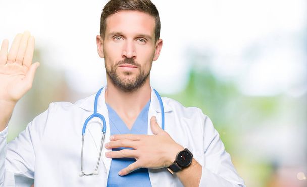 Komea lääkäri mies yllään lääketieteellinen univormu yli eristetty tausta Vannoo käsi rinnassa ja avoin kämmen, jolloin uskollisuus lupaus vala
 - Valokuva, kuva