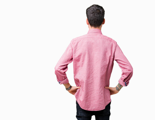 Fiatal jóképű férfi rózsaszín inget visel elszigetelt háttérben álló hátra keres el karral a test felett - Fotó, kép