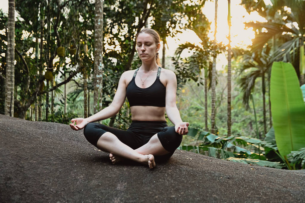 young girl doing yoga at sunset in jungle - 写真・画像