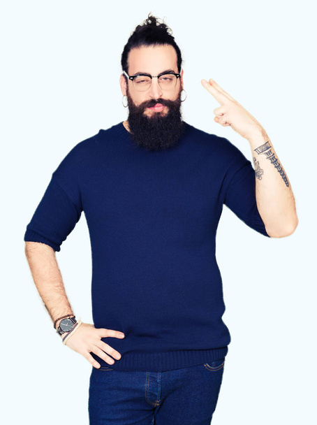 Jeune homme hipster aux cheveux longs et barbe portant des lunettes Tir et se suicider en pointant la main et les doigts vers la tête, geste suicidaire
. - Photo, image