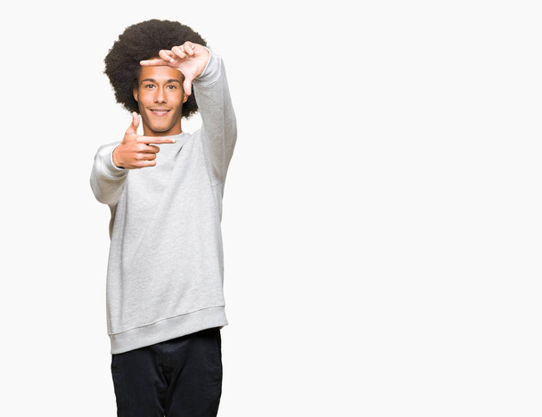 Young african american man with afro hair wearing sporty sweatshirt smiling making frame with hands and fingers with happy face. Creativity and photography concept. - Fotoğraf, Görsel