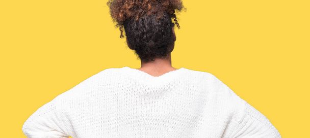 Belle jeune femme afro-américaine vêtue d'un pull d'hiver sur fond isolé regardant vers l'arrière avec les bras sur le corps
 - Photo, image