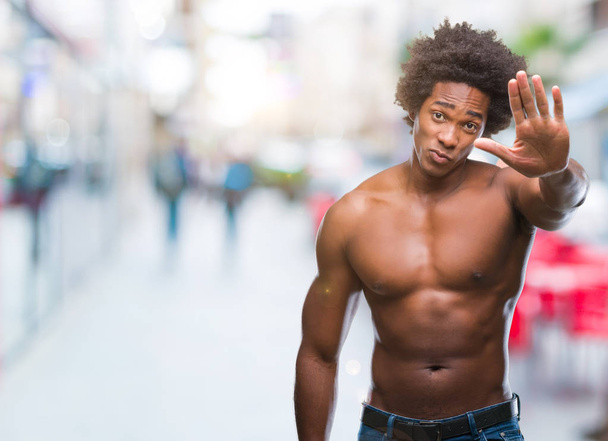 Afro Amerikaanse shirtless man naakt lichaam tonen over geïsoleerde achtergrond stop doen zingen met de palm van de hand. Waarschuwing expressie met negatieve en ernstige gebaar op het gezicht. - Foto, afbeelding