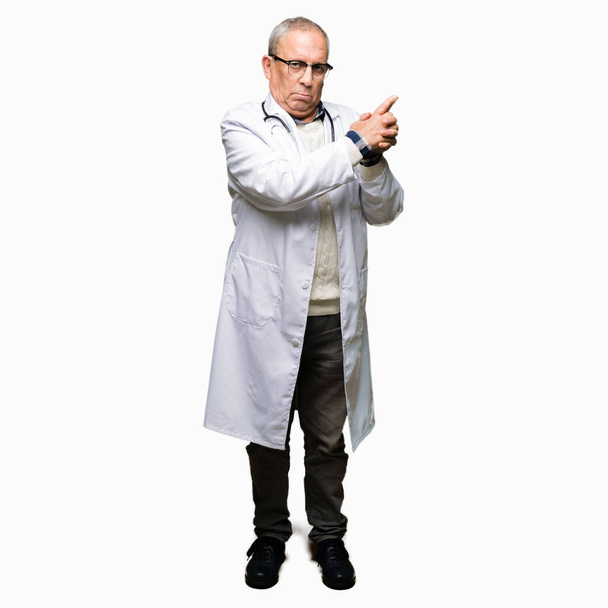 Handsome senior doctor man wearing medical coat Holding symbolic gun with hand gesture, playing killing shooting weapons, angry face - Photo, Image